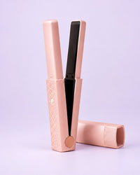 Pink cordless mini flat iron standing open beside its cap