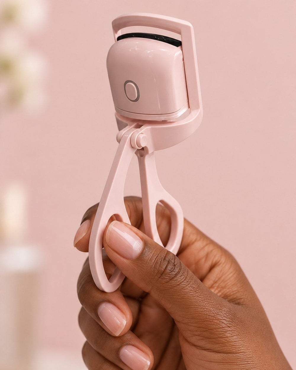 The heated curler held by its handles in one hand, the size of a regular lash curler