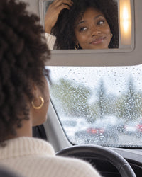 Woman in a parked car checking her frizzy fringe in the visor mirror on a rainy day
