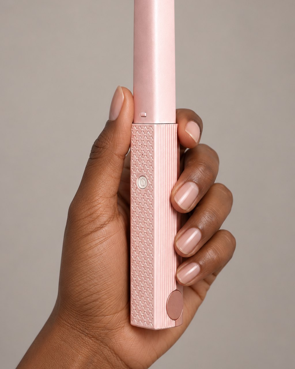 The closed pink mini flat iron held upright in one hand, showing its slim size