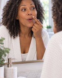 Woman leaning into a window-lit mirror, noticing fine hair on her upper lip