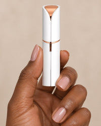 The facial hair remover held between thumb and fingers, the size of a lipstick