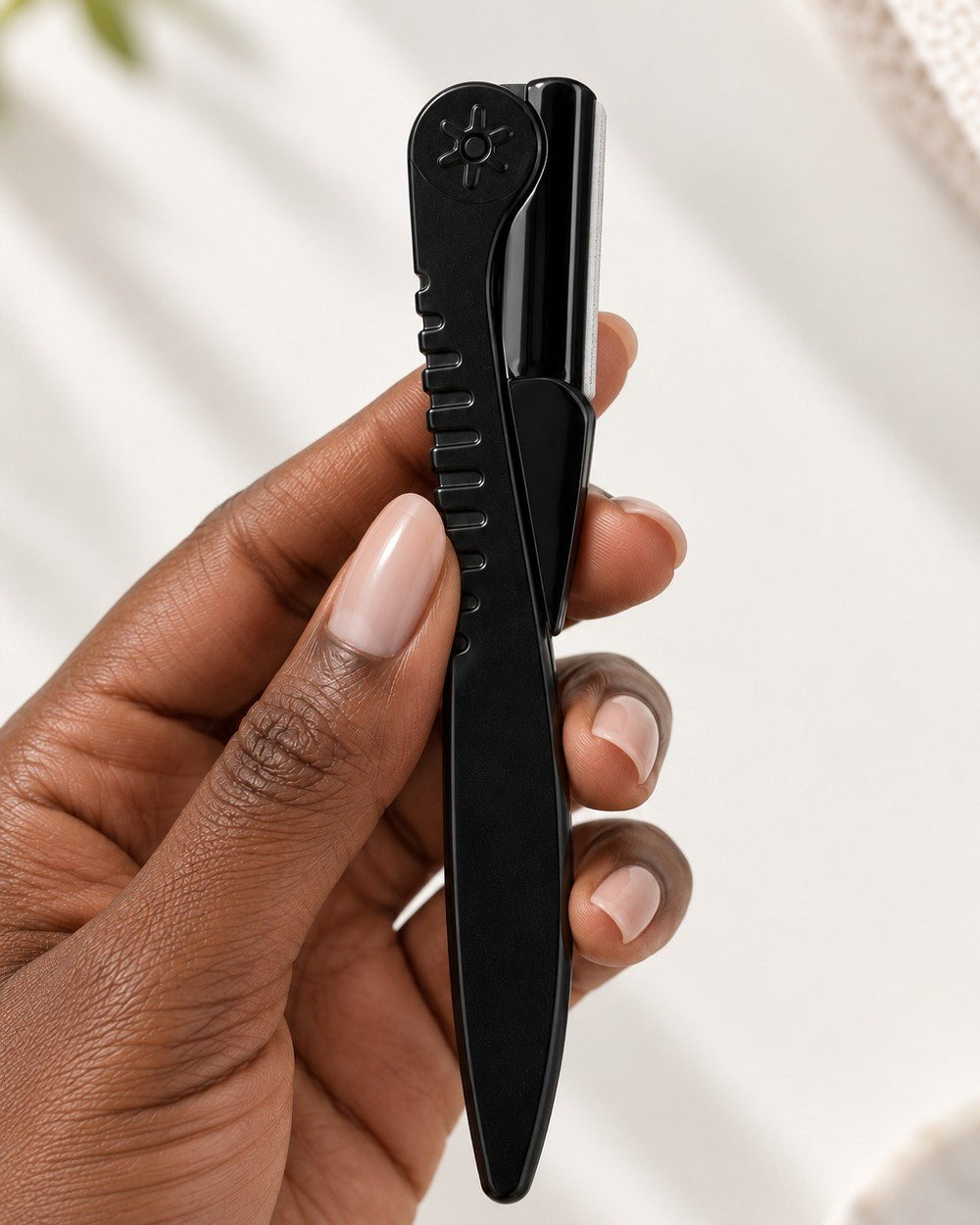 The razor folded flat between two fingers, about the length of a pen