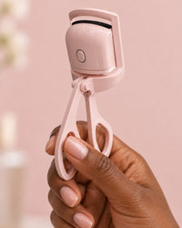 The heated curler held by its handles in one hand, the size of a regular lash curler