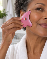 Woman gliding the pink gua sha along her cheekbone, its heart light glowing red