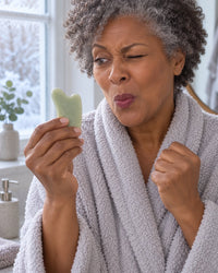 Woman wincing at an icy stone gua sha on a cold morning