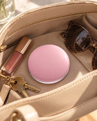 Pink compact mirror next to a lipstick and keys in an open handbag