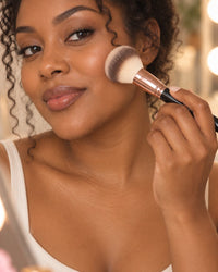 Woman buffing foundation onto her cheek with a fluffy face brush