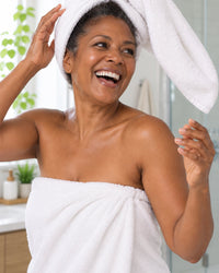 A woman laughs as a heavy bath towel turban slides off her head