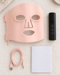 Silicone LED mask, handheld controller, cables and manual laid out from above