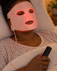 Woman lying back with eyes closed, the pink silicone mask glowing red on her face