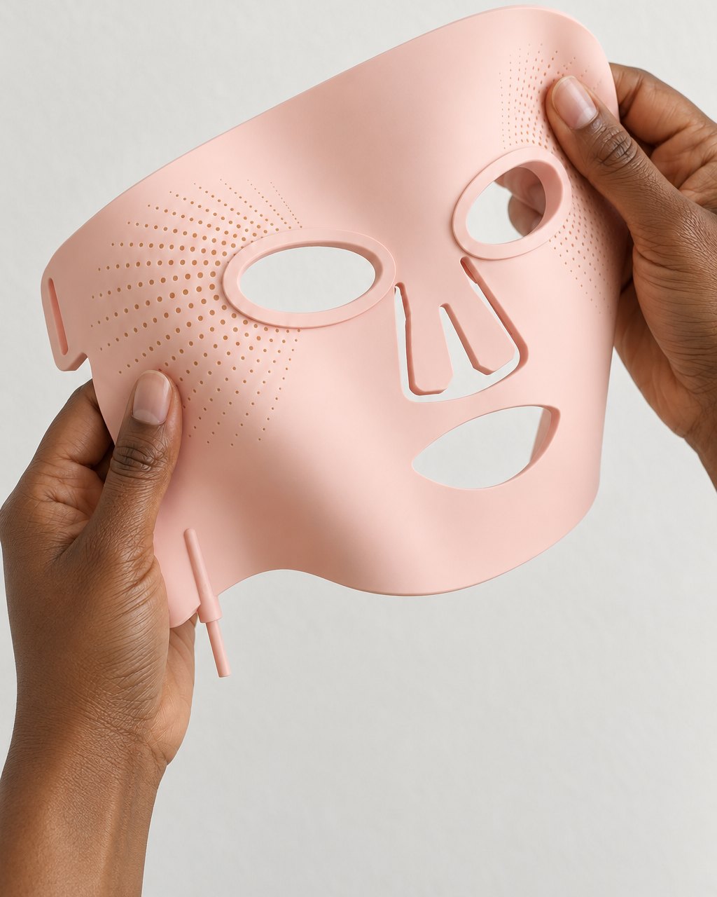 Silicone LED mask held in two hands and gently bent to show how flexible it is