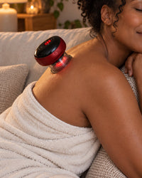 Woman relaxing on a sofa with the red cupping massager on the back of her shoulder