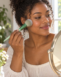 Woman sweeping powder onto her cheek with a fluffy sage green brush
